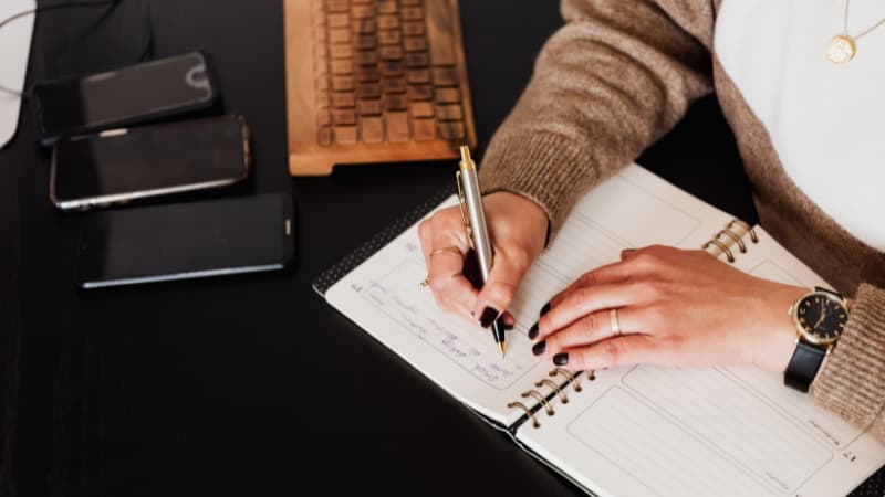 Woman with black nail polish sits at her desk writing in her journal