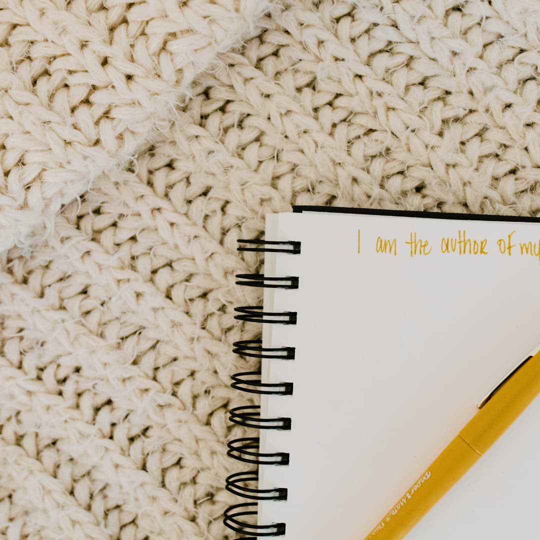 A journal sits on a woven rug, with "I am the author of my" written at the top of the page in yellow
